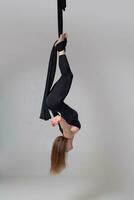 Beautiful girl in a black sport suit is performing an acrobatic elements in a studio. photo