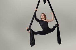 hermosa niña en un negro deporte traje es ejecutando un acrobático elementos en un estudio. foto