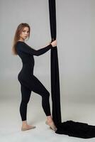 Beautiful girl in a black sport suit is performing an acrobatic elements in a studio. photo
