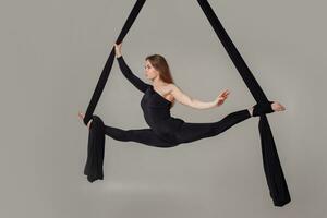 Beautiful girl in a black sport suit is performing an acrobatic elements in a studio. photo