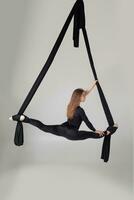 Beautiful girl in a black sport suit is performing an acrobatic elements in a studio. photo