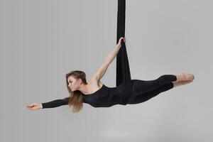 Beautiful girl in a black sport suit is performing an acrobatic elements in a studio. photo