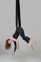 Beautiful girl in a black sport suit is performing an acrobatic elements in a studio. photo