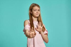 estudio retrato de un hermosa niña rubia adolescente en un rosado camiseta posando terminado un azul antecedentes. foto