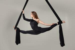 Beautiful girl in a black sport suit is performing an acrobatic elements in a studio. photo