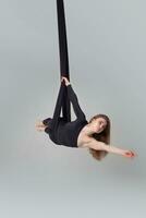 Beautiful girl in a black sport suit is performing an acrobatic elements in a studio. photo