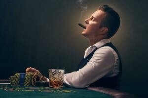 Wealthy man is smoking a cigar and playing poker with an excitement at a casino on black background. photo
