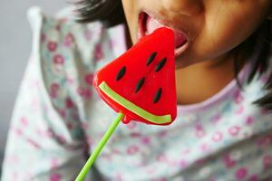 child is licking colorful candy on stick, photo