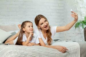 Indoor portrait of a beautiful mother with her charming little daughter posing against bedroom interior. photo