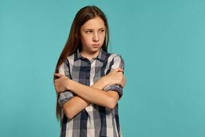 Beautiful teenage girl in a casual checkered shirt is posing against a blue studio background. photo