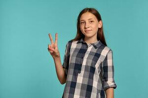 Beautiful teenage girl in a casual checkered shirt is posing against a blue studio background. photo