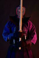 cerca arriba disparo, kendo combatiente vistiendo en un armadura, tradicional kimono, casco practicando marcial Arte con shinai bambú espada, negro antecedentes. foto
