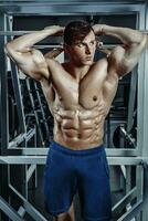 hermoso hombre con grande músculos, posando a el cámara en el gimnasio foto