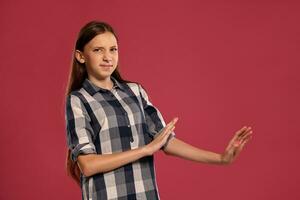 Beautiful teenage girl in a casual checkered shirt is posing against a pink studio background. photo