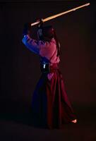 Close up shot, Kendo fighter wearing in an armor, traditional kimono, helmet practicing martial art with shinai bamboo sword, black background. photo