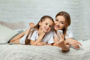 Indoor portrait of a beautiful mother with her charming little daughter posing against bedroom interior. photo