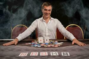 Handsome emotional man is playing poker sitting at the table in casino. photo