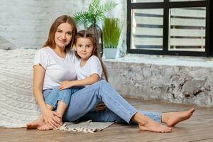 Indoor portrait of a beautiful mother with her charming little daughter posing against bedroom interior. photo