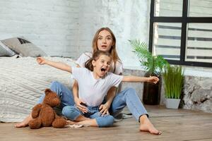 Indoor portrait of a beautiful mother with her charming little daughter posing against bedroom interior. photo