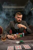 hermoso barbado hombre es jugando póker sentado a el mesa en casino. foto