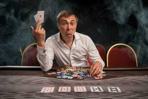 Handsome emotional man is playing poker sitting at the table in casino. photo