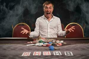 Handsome emotional man is playing poker sitting at the table in casino. photo