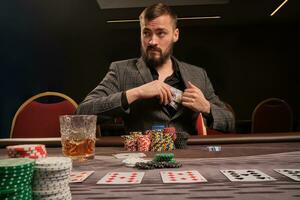 Handsome bearded man is playing poker sitting at the table in casino. photo