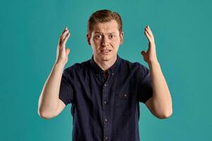 Close-up portrait of a ginger guy in navy t-shirt posing on blue background. Sincere emotions. photo