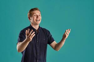 Close-up portrait of a ginger guy in navy t-shirt posing on blue background. Sincere emotions. photo