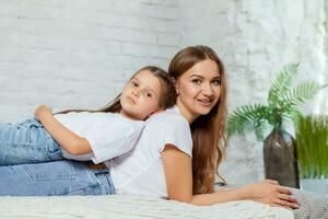 interior retrato de un hermosa madre con su encantador pequeño hija posando en contra dormitorio interior. foto