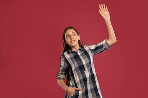 Beautiful teenage girl in a casual checkered shirt is posing against a pink studio background. photo