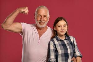 Beautiful teenage girl with her grandfather posing against a pink studio background. photo
