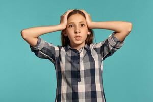 Beautiful teenage girl in a casual checkered shirt is posing against a blue studio background. photo