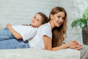 interior retrato de un hermosa madre con su encantador pequeño hija posando en contra dormitorio interior. foto