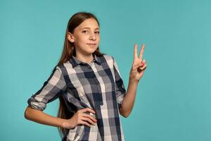 Beautiful teenage girl in a casual checkered shirt is posing against a blue studio background. photo