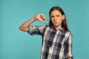 Beautiful teenage girl in a casual checkered shirt is posing against a blue studio background. photo