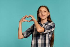 Beautiful teenage girl in a casual checkered shirt is posing against a blue studio background. photo