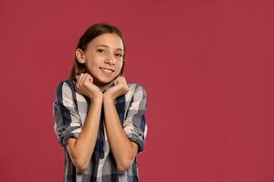 Beautiful teenage girl in a casual checkered shirt is posing against a pink studio background. photo