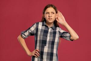 Beautiful teenage girl in a casual checkered shirt is posing against a pink studio background. photo