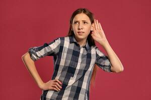 Beautiful teenage girl in a casual checkered shirt is posing against a pink studio background. photo