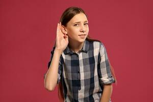 Beautiful teenage girl in a casual checkered shirt is posing against a pink studio background. photo