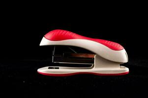 a red and white stapler on a black background photo