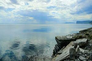 a rocky shore with a large body of water and clouds photo