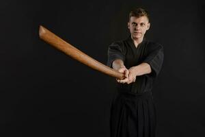 Kendo guru wearing in a traditional japanese kimono is practicing martial art with the shinai bamboo sword against a black studio background. photo