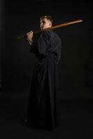 kendo gurú vistiendo en un tradicional japonés kimono es practicando marcial Arte con el shinai bambú espada en contra un negro estudio antecedentes. foto