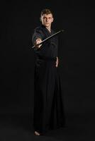 Kendo guru wearing in a traditional japanese kimono is practicing martial art with the shinai bamboo sword against a black studio background. photo