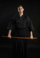 Kendo guru wearing in a traditional japanese kimono is practicing martial art with the shinai bamboo sword against a black studio background. photo