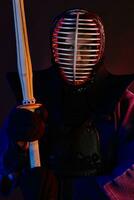 Close up shot, Kendo fighter wearing in an armor, traditional kimono, helmet practicing martial art with shinai bamboo sword, black background. photo