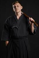 Kendo guru wearing in a traditional japanese kimono is practicing martial art with the shinai bamboo sword against a black studio background. photo