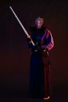 Close up shot, Kendo fighter wearing in an armor, traditional kimono, helmet practicing martial art with shinai bamboo sword, black background. photo